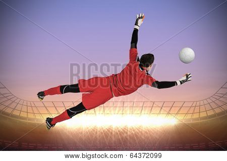 Fit goal keeper jumping up against large football stadium with spotlights at sunrise