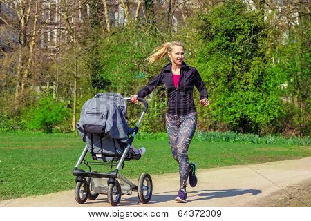 Smiling young woman pushing baby buggy while exercising in a park