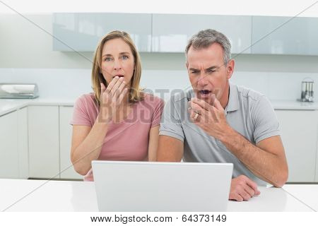 Shocked couple using laptop in the kitchen at home