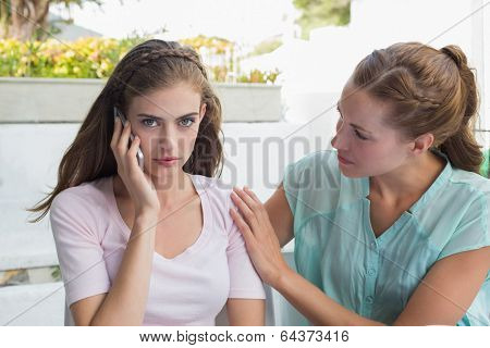 Young woman consoling a sad friend while shes on call in the cafÃ?ÃÂ©