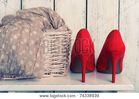 Red women shoes and scarf on bench on wooden background