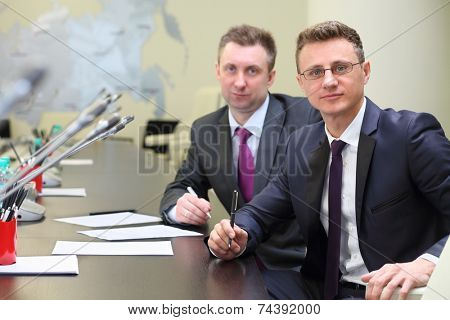 Portrait of two businessmen at negotiating table in conference hall