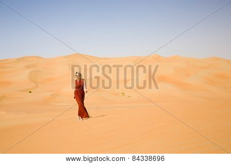 Long dressed woman walks in desert