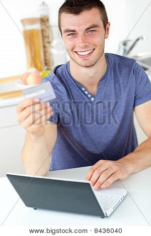 Carismático jovem segurando uma placa usando seu Laptop na cozinha