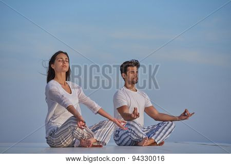 young couple practicing yoga at sunset in modern home terace with ocean and sunset in background