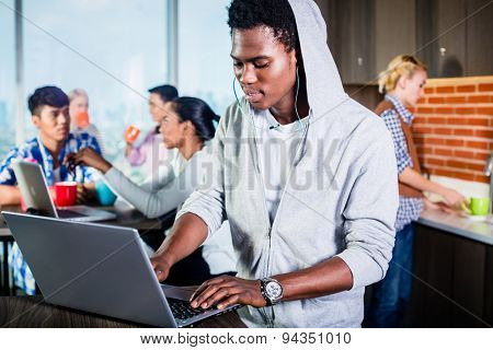 Black programmer in lounge of IT start-up coding software on his laptop, colleagues in the background