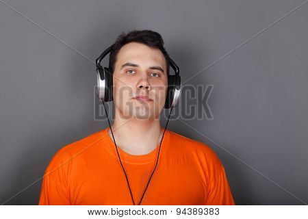 Beautiful Young Man In Headphones And Orange T-shirt In Grey Studio