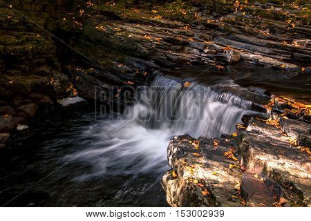 Water flows gently over rocks adorned with Autumn leaves at Raymondskill Falls near Milford, PA