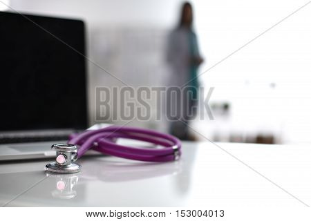 Laptop and stethoscope on the desk doctors standing in the background.