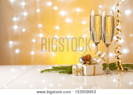 Two glasses with champange, fir tree branch, gift boxes and christmas decorations on a yellow background with lights of garland.  New year and Christmas.