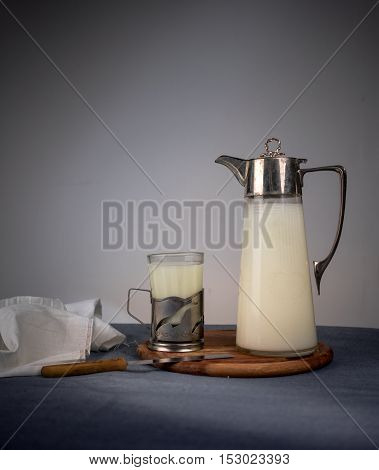 ancient jug with milk and a glass on a wooden table.