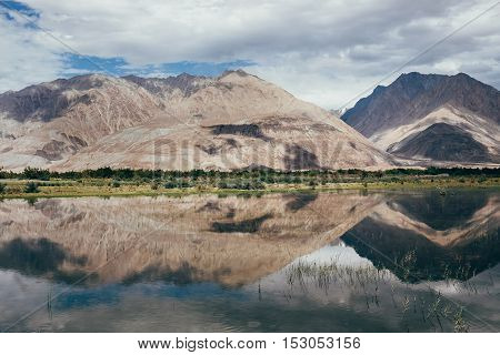 Mountain peaks reflect in water Nubra river