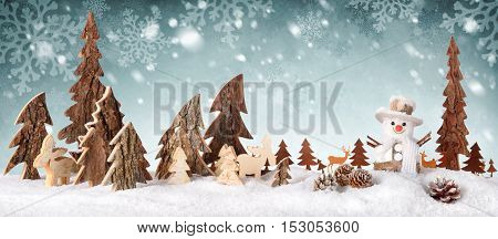 Wooden decoration arranged as a cute winter scene with a snowman conifer trees Christmas star animals and snow on a snowflakes background