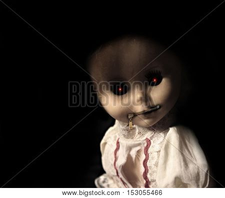 Vintage evil spooky doll with zipped mouth. On black background