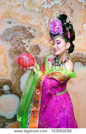 Sweet Chinese girl in violet traditional dress with flower against marble wall