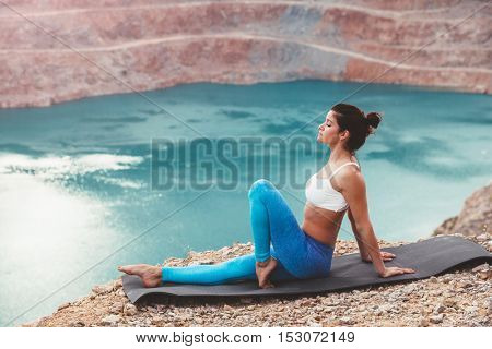 Young sporty girl wearing blue activewear stretching outdoors. Woman training yoga pose on mountain hill, calm and silent view.