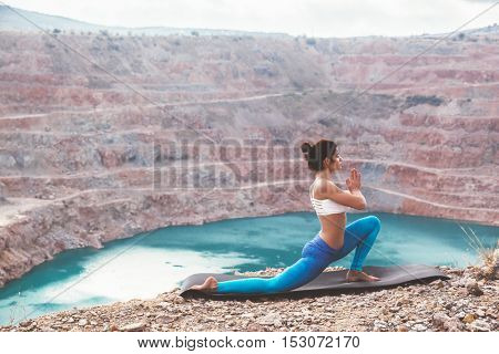 Young sporty girl wearing blue activewear stretching outdoors. Woman training yoga pose on mountain hill, calm and silent view.