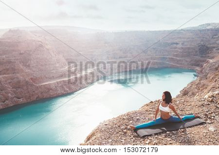 Young sporty girl wearing blue activewear stretching outdoors. Woman training yoga pose on mountain hill, calm and silent view.