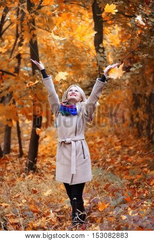 laughing girl with long blonde hair throws leaves in autumn park. Happy woman playing with autumn leaves in forest. Happiness carefree leisure concept. Blond woman relaxing in autumn park throwing leaves up in the air. Beautiful girl in orange forest foli