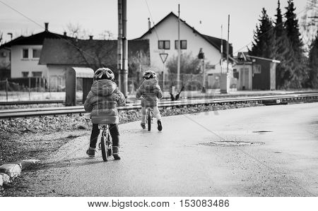 Twins children riding balance bikes on the road with helmet. Young toddlers with in bicycle helmet are riding bikes in the winter on the road with railroad tracks near by