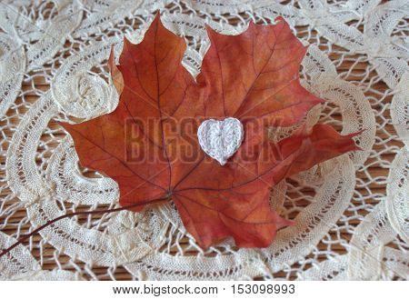 Dry autumn maple leaf and crochet heart on wooden background. Herbarium. Artistic original backdrop place for text copy space