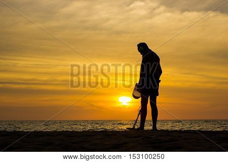 a treasure hunter with Metal detector on sunset on the beach