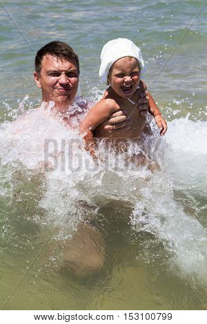 man father and daughter a little girl swimming in the sea in the waves splashing happiness joy laughter summer vacation