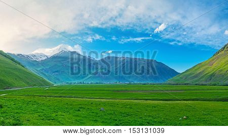 The juicy greenery of the meadows in Sno valley with the uncovered peak of Kazbek Mount on background Kazbegi Georgia.
