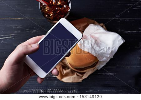 Cheeseburger in the paper container with paper napkins on a dark wooden background with moblie phone
