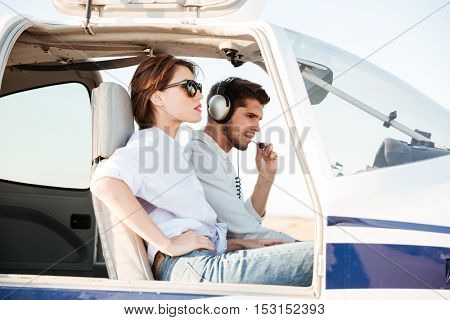 Young pilot and beautiful stewardess sitting together inside airplane cabin waiting for take off