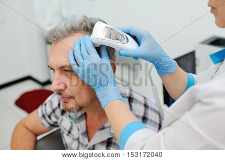 diagnostics hair and scalp. Trihoskopiya. Doctor examine patient male hair a special apparatus