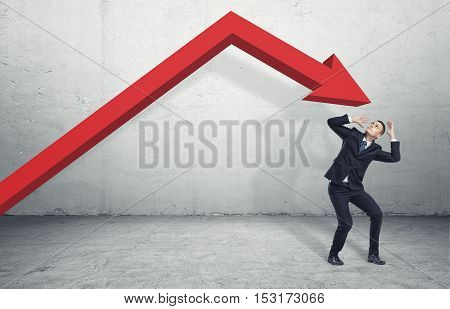 Businessman standing on the floor in a desparate pose under the giant red arrow aiming down at him, on the grey background. Business and management. Problems and failures. Dealing with crisis.