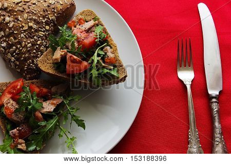 bread cut in half with tuna tomato and arugula on a red tablecloth