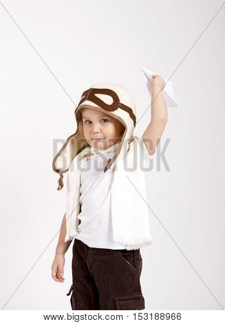 happy kid playing with paper airplane. studio photo. aviator hat and scarf