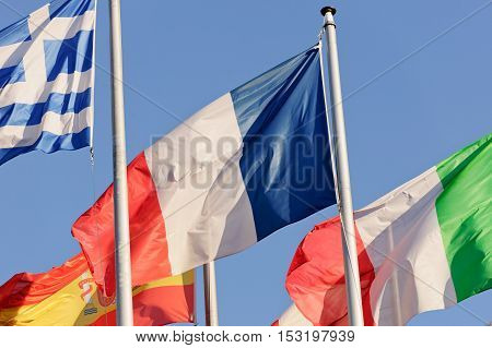 French National Flag surrounded by Italian Flag Geece Flag Spain Flag against blue sky in front of European Parliament