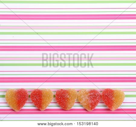 five jelly candies in heart shape on striped multicolored background Top view. Valentine's Day Concept