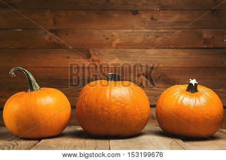 Three fresh orange pumpkin on wooden background closeup. Vintage toned