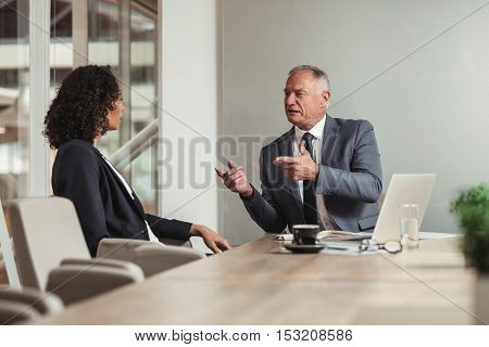 Mature businessman and young work colleague discussing business while sitting together at a table in an office boardroom