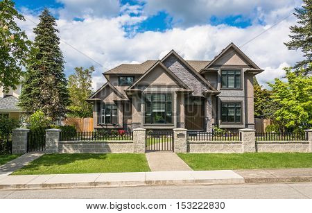 Modern luxury residential house with tile paved pathway on cloudy sky background. High end family home with big front yard behind stone wall fence