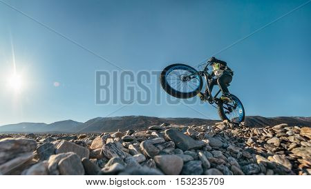 Fatbike also called fat bike or fat-tire bike - Cycling on large wheels. Traveller athlete jumps on the bike on the rocky shore of Lake Baikal, with mountain views.