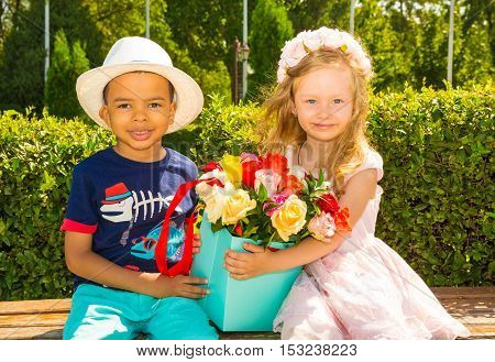 Black african american boy kid gives flowers to girl child on birthday. Little adorable children in park. Childhood and love.