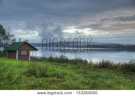 Vintage Russian smoke sauna log cabin on a river shore.