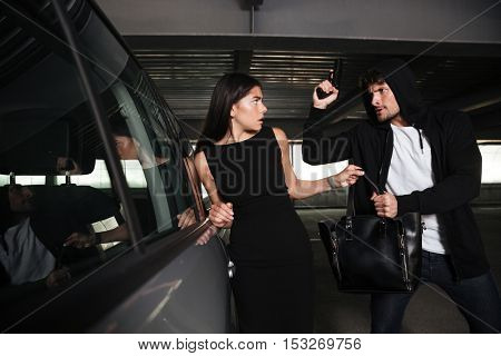 Angry man thief in hoodie stealing woman bag and treatening to her with gun on car parking