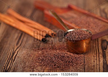 grated dark chocolate in copper measure pan on wooden background