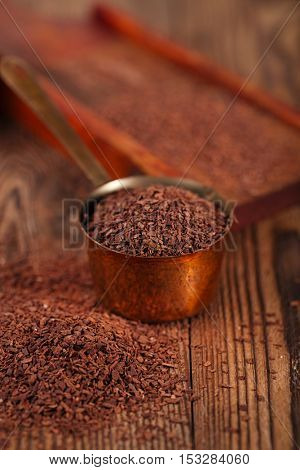 grated dark chocolate in copper measure pan on wooden background