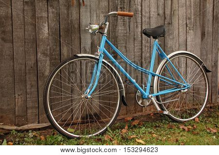 Classic vintage retro city bicycle in blue leaning against wood texture fence.