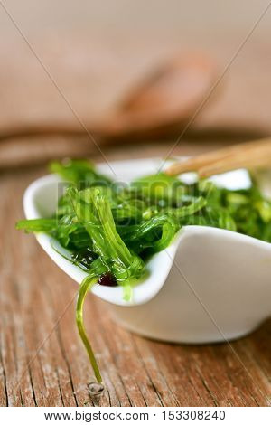 goma wakame or seaweed salad in a white ceramic bowl, on a rustic wooden table