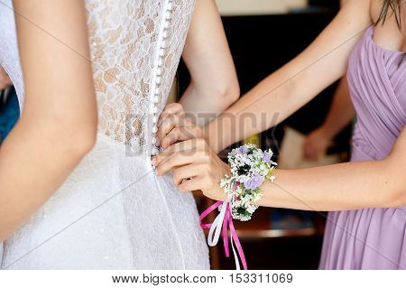 bride wearing wedding white dress. helping the bride to put her. bridesmaids dress laces on the back. tying bow