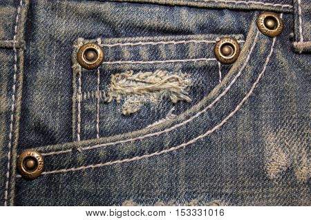 Old dirty blue jeans with holes and scrapes. Jeans pocket with bronze buttons. Rivets with sign JEANS in rim.