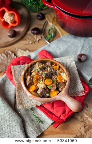 Stewed beef in a clay pot on a rustic tabletop.